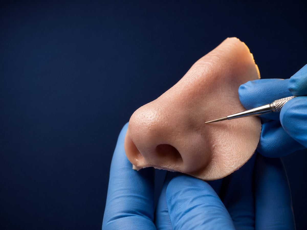 Custom hand-sculpted silicone nasal prosthesis with lifelike skin texture, held in a clinician's gloved hands during final detailing